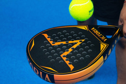 victoria padel tear druppel racket 3k carbon zwart oranje productfoto blauwe achtergrond bal actiefoto