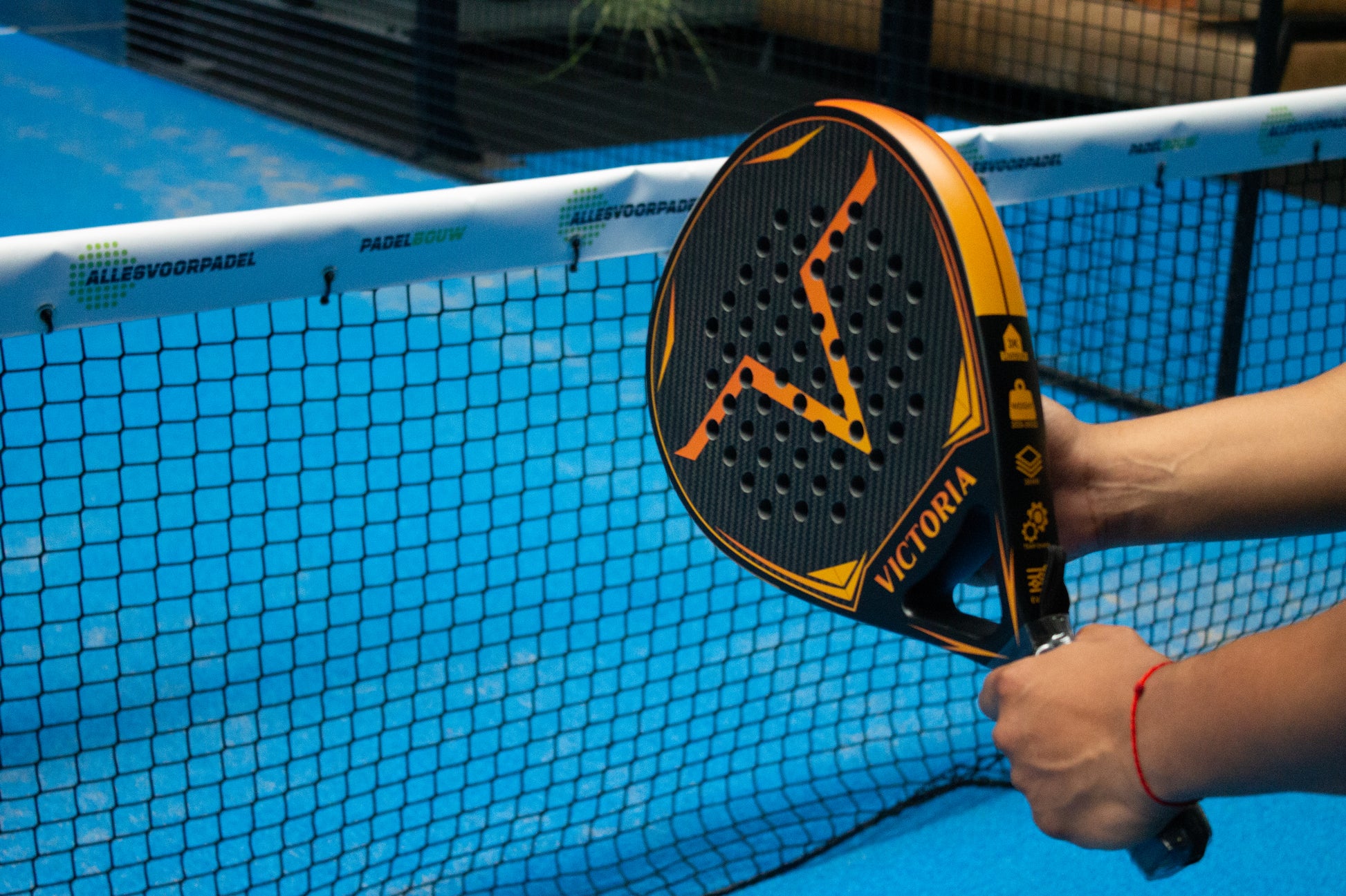 victoria padel tear druppel racket 3k carbon zwart oranje productfoto blauwe achtergrond met hek actiefoto